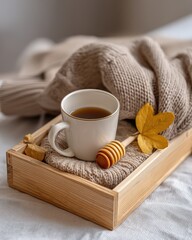 Flat lay of a wooden tray with honey dipper, dried leaves, a teacup, and a knitted coaster, soft shadows, cozy aesthetic