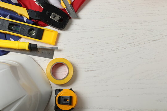Image of work gloves, tools and American flag on wooden surface symbolizing Labor Day in the USA

