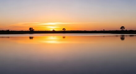Calm waters reflecting an orange and yellow sunset with trees on the horizon