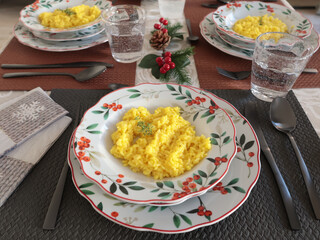 Table setting with bright tableware, berries, and twigs. Saffron risotto on plate. Traditional Italian food. Aesthetics and lifestyle. Interior design. 