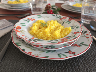 Table setting with bright tableware, berries, and twigs. Saffron risotto on plate. Traditional Italian food. Aesthetics and lifestyle. Interior design. 