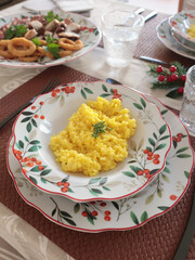 Table setting with bright tableware, berries, and twigs. Saffron risotto on plate. Traditional Italian food. Aesthetics and lifestyle. Interior design. 