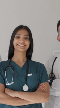 Vertical video. Diverse confident medical team of doctors and nurse in hospital uniforms, arms crossed, smiling and looking at camera