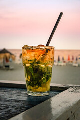 Mojito cocktail on beach bar at sunset. Summer vacation concept, refreshing rum drink with mint and ice, sea in background