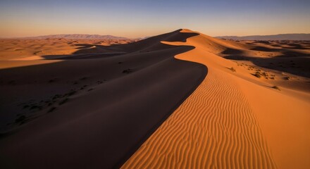 Aerial view of a vast desert landscape featuring sand dunes at golden hour, with mountains