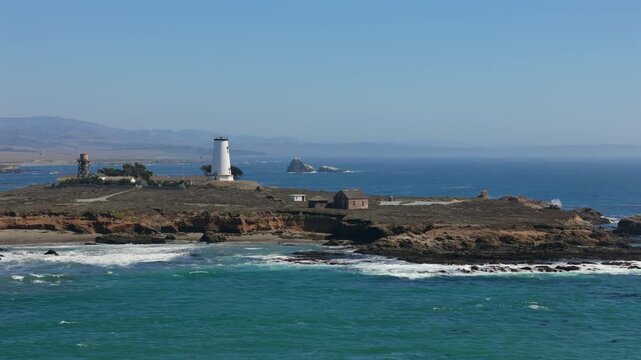 Scenic coastal view of Pigeon Point Lighthouse near San Simen California standing on rocky shore above Pacific Ocean under clear blue sky symbolizing maritime history and natural beauty