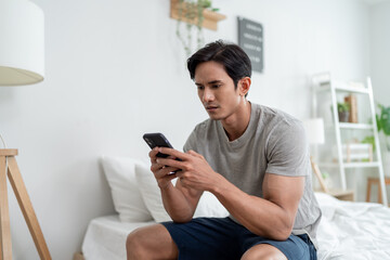 Asian depressed young man chat on mobile phone in bedroom at home.
