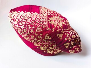 A traditional peci or songkok Manuk Meghem Tapis from Lampung, Indonesia, displayed on a white background. The cap features red woven fabric with gold thread patterns and traditional motifs.