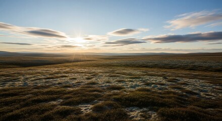 A serene landscape at dawn, sunlight breaks through the clouds. A vast, blurred grassy plain