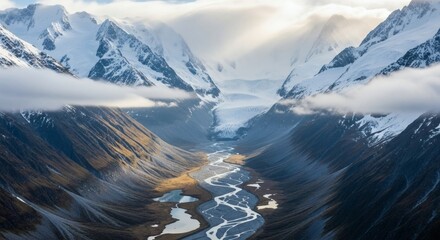 Dramatic aerial view of a glacial valley, snow-capped peaks, river, clouds, and sunlight