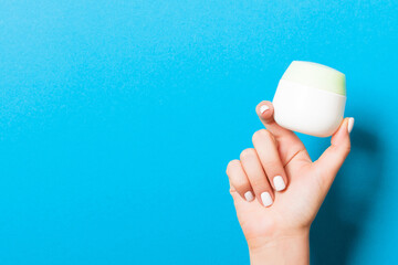 Female hand holding cream bottle of lotion isolated. Girl give jar cosmetic products on blue background