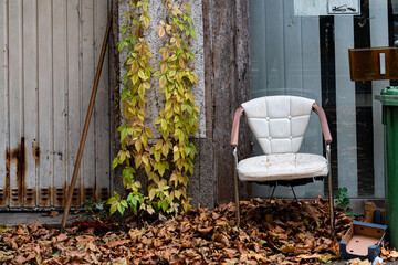 Old abandoned chair surrounded by autumn leaves in urban setting