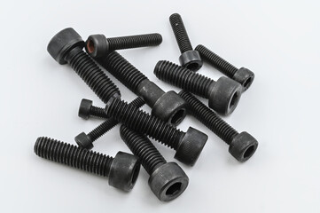 Close-up of several black metric socket head cap screws arranged on a white background, used in mechanical and industrial assembly.