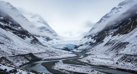 A winding river flows between snowy, mountainous terrain, leading towards a glacier under a cloudy sky