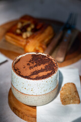 A cup of hot cocoa topped with cocoa powder served with pastry and cookie on wooden plate in cozy coffee shop atmosphere.