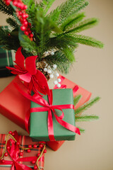 Green and red festive gifts tied with ribbon near evergreen branches and red berries