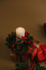 Christmas candle burning on pine wreath with festive gift boxes and red berries