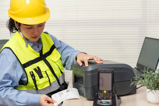 Asian female engineer uses a laptop or notebook to print barcode stickers on a barcode printer.
