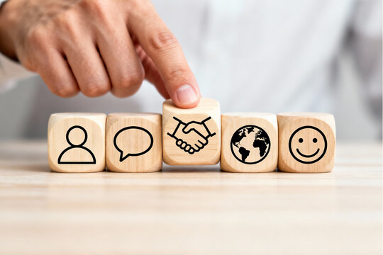 Global Collaboration and Communication Success: Hand pressing on wooden blocks with person, speech bubble, handshake, globe and smiley icons, symbolizing positive outcomes from interpersonal to intern