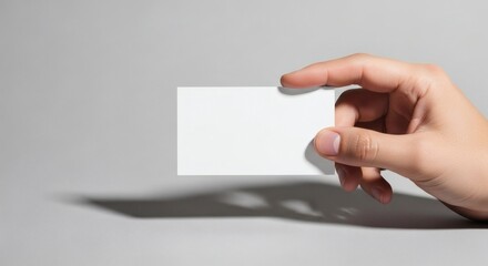 Hand holding a blank white business card for mockup on a grey background with a shadow.