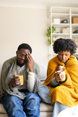 Sick couple suffering from cold or flu drinking hot beverage on sofa