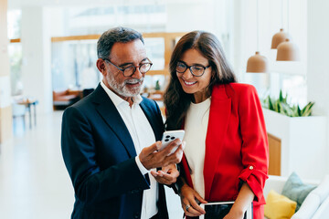 Senior professionals smiling and discussing using a smartphone indoors