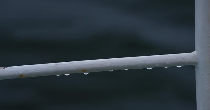 Raindrops hang on white metal railing of sailing vessel closeup. Water drips from border bar on yacht deck during sea voyage on stormy day