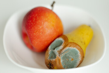 Moldy pear with mold and fresh apple on plate