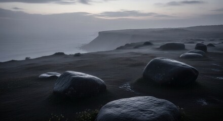 Obraz premium A rugged coastal scene with large stones, mist, and a distant headland under a cloudy sky