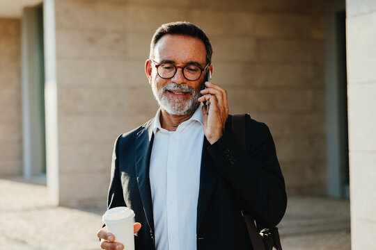 Businessman using phone and holding coffee cup in urban setting