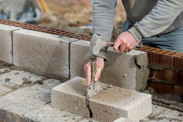 Bricklayer builder using chisel to break bricks and blocks on construction site