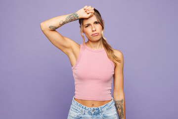 Young sad sick ill tired weary woman she wearing pink tank top casual clothes hand on forehead looking camera isolated on plain pastel light purple wall background studio portrait. Lifestyle concept.