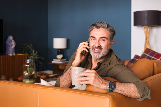 Smiling man talking on phone with coffee on sofa at home
