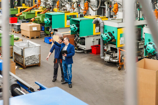 Employees inspecting machinery in plastics production hall