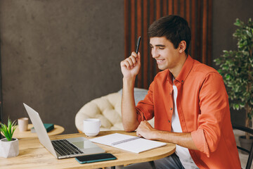 Side view young IT man wear casual clothes work or study on laptop pc computer sit alone at table...