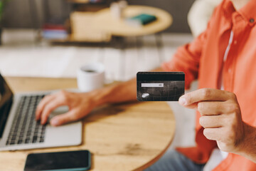 Close up cropped man use laptop pc computer hold credit card speak on cell phone sit at table in coffee shop cafe relax rest in restaurant in free time indoor Freelance mobile concept Focus on object