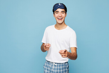 Calm young man wear pyjamas jam sleep eye mask rest relax at home point index finger camera on you motivate encourage isolated on plain pastel light blue cyan background. Good mood night nap concept