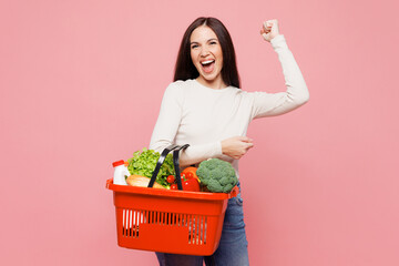 Young woman wear white casual clothes hold orange basket with food products do winner gesture...