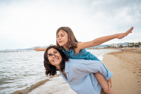 Happy mother giving piggyback ride to daughter at beach