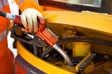 Close-up of Construction worker in safety gloves filling excavator with diesel fuel on building site