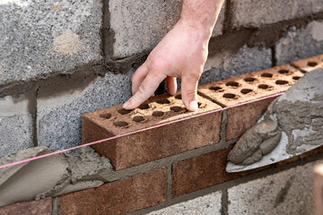 Bricklayer builder working laying red bricks and blocks on construction site