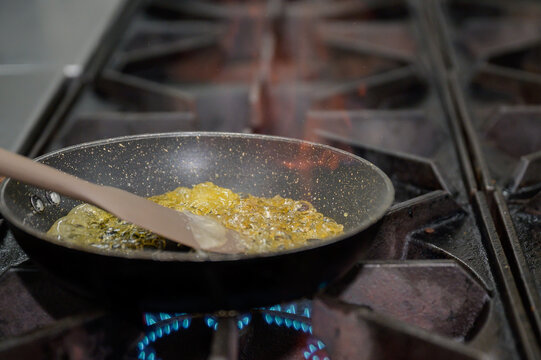 Close-up cooking process of Crepes Suzette with orange sauce, sugar caramelizing and flambe technique in a professional kitchen, fine dining dessert preparation.