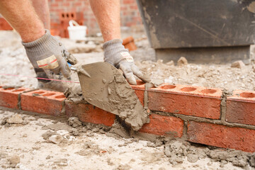 Bricklayer builder working laying red bricks and blocks on construction site