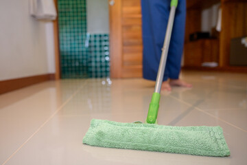 A close-up of a green microfiber mop cleaning a glossy indoor tile floor was taken in soft natural light with a shallow depth of field and surface reflection.