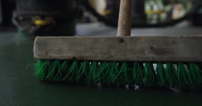 Sweeping rough floor with old brush on ship vessel deck closeup. Cleaning dirty surface with plastic wooden broom at maritime transport