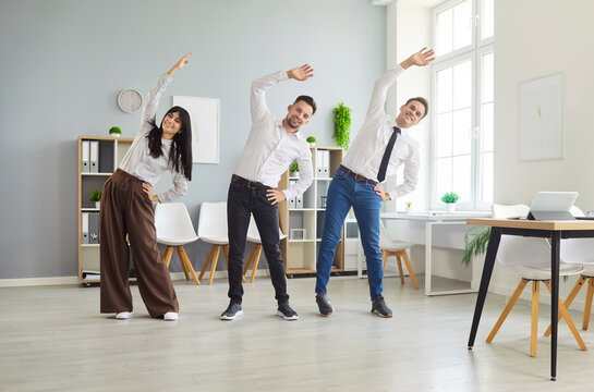 Fototapeta Three smiling coworkers perform synchronized side bends in a bright office, facing the camera during a wellness break. Simple stretching builds teamwork and flexibility. Smiles boost energy.