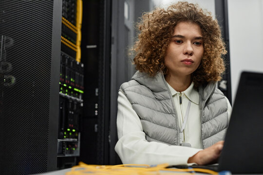IT professional with curly hair working on laptop in data center