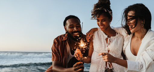 Friends holding sparkler together celebrating on a beach at sunset
