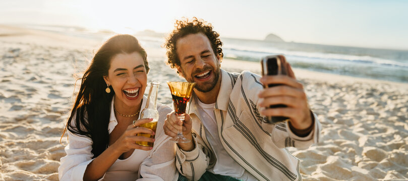 Couple enjoying drinks and capturing memories on the beach at sunset