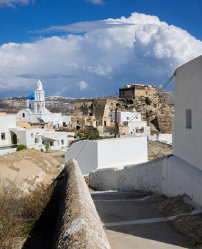 Narrow Cycladic Alley Leading to the Historic Venetian Castle Ruins and Blue Domed Church in Akrotiri, Santorini, Greece. 7 October 2025